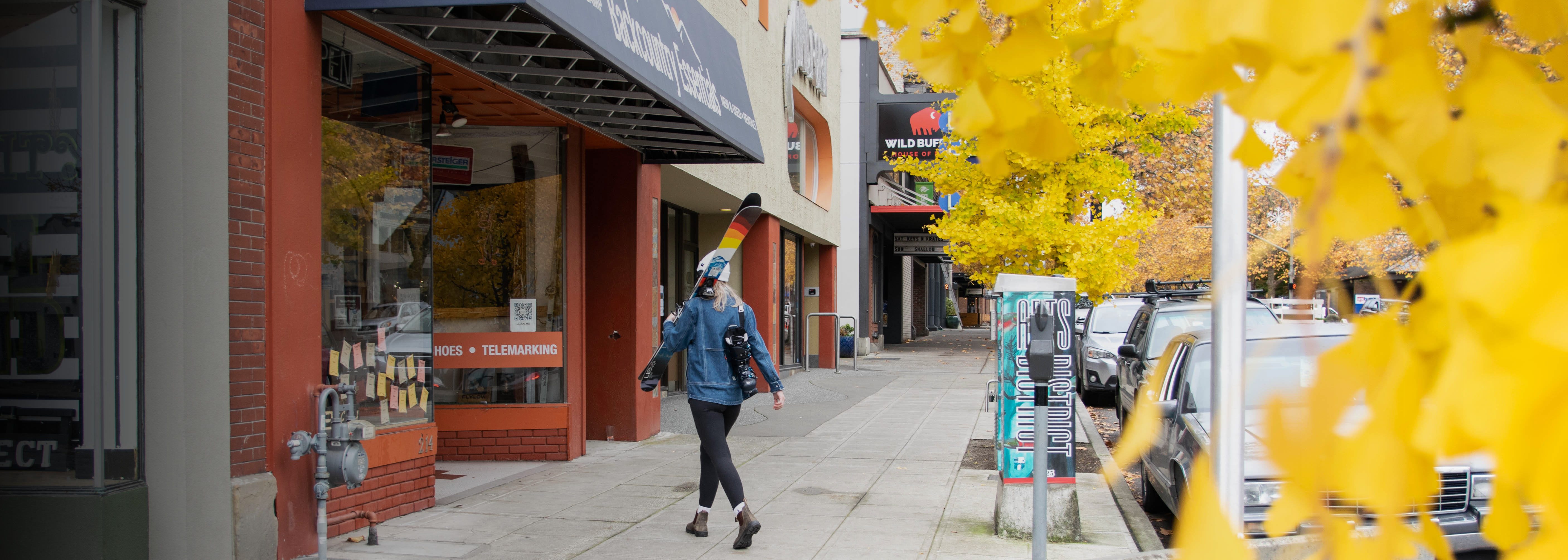 A customer walks into Backcountry Essentials with ski gear.